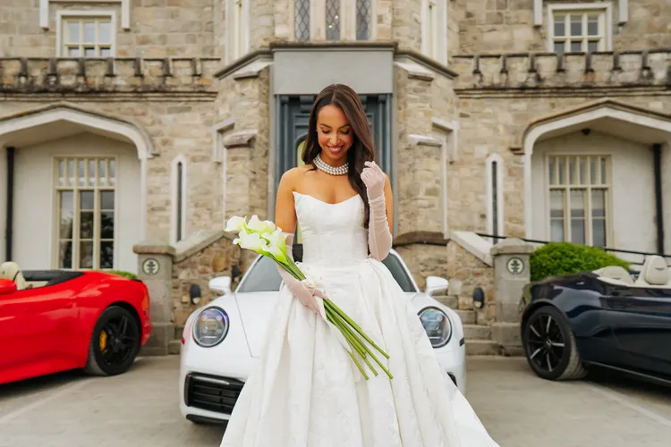 Bride with wedding bouquet standing beside luxury wedding cars